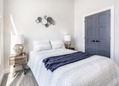 Thumbnail 25 of 37 - A bedroom with a bed, nightstand, and lamp.