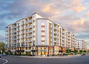 Thumbnail 1 of 37 - A large apartment building with a parking lot in front.