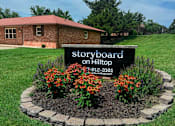 Thumbnail 1 of 14 - A sign for Storyboard on Hilltop stands in a flowerbed.