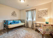 Thumbnail 11 of 11 - A bedroom with a bed, chair, and a wall hanging.