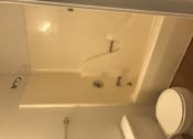 Thumbnail 27 of 51 - A white toilet is next to a bathtub with a shower head.