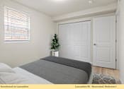 Thumbnail 19 of 24 - A bedroom with a bed, a window with blinds, a plant, and two doors.