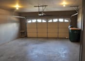 Thumbnail 51 of 51 - A large empty garage with a closed door and a green trash can.