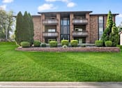 Thumbnail 2 of 24 - the front of a brick apartment building with green grass and shrubs