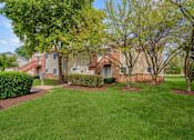 Thumbnail 4 of 11 - A grassy area in front of a building with a tree and bushes.