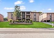 Thumbnail 5 of 24 - the front of a brick apartment building with a lawn and trees