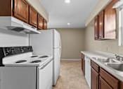 Thumbnail 11 of 14 - A kitchen with a white stove and refrigerator, brown cabinets, and a tiled floor.