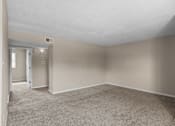 Thumbnail 8 of 14 - A large, empty room with carpeted flooring and a doorway leading to another room.