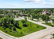 Thumbnail 3 of 56 - A view of a roundabout with a grassy area in the middle and buildings in the background.