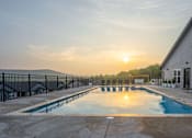 Thumbnail 9 of 38 - A sunset view of a pool with lounge chairs and a building in the background.