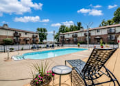 Thumbnail 6 of 6 - A pool area with chairs and a table in front of apartment buildings.