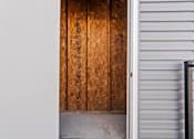 Thumbnail 26 of 64 - A wooden door with a white wall on the left and a white wall with a black railing on the right.