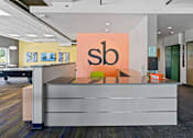 Thumbnail 25 of 56 - A reception area with a white desk and a sign with the letters "sb" on it.