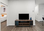 Thumbnail 20 of 38 - A black television is on a wooden stand in a white room.