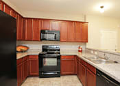 Thumbnail 16 of 23 - A kitchen with brown cabinets and black appliances.