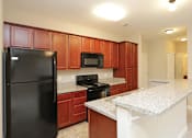 Thumbnail 19 of 23 - A kitchen with brown cabinets and a black refrigerator.