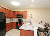 Thumbnail 9 of 23 - A kitchen with brown cabinets and a black refrigerator.