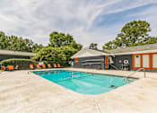Thumbnail 19 of 25 - A large outdoor swimming pool surrounded by orange chairs and trees.