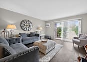 Thumbnail 5 of 32 - Living room at Renaissance at Carol Stream featuring grey couches and a large wall clock in Carol Stream, IL.