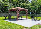 Thumbnail 17 of 18 - A gazebo with picnic tables is surrounded by a fence and trees.