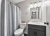 Thumbnail 11 of 32 - Bathroom at Renaissance at Carol Stream featuring a white toilet, white sink, and grey shower curtain in Carol Stream, IL.