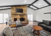 Thumbnail 16 of 34 - A living room with a stone fireplace and a flat screen TV mounted above it.