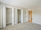 Thumbnail 12 of 21 - A room with white walls and a carpeted floor with four open closets.