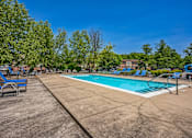 Thumbnail 17 of 21 - A large outdoor swimming pool surrounded by trees and lounge chairs.