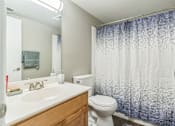 Thumbnail 6 of 20 - A bathroom with a white sink, toilet, and a blue shower curtain.