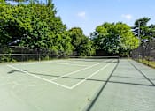 Thumbnail 28 of 30 - A tennis court surrounded by trees and fencing.