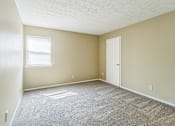 Thumbnail 10 of 20 - A room with a carpeted floor, a door, and a window.