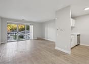 Thumbnail 4 of 26 - A spacious room with wooden flooring and a kitchen area in the background.