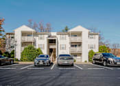 Thumbnail 30 of 32 - A white apartment building with cars parked in front.