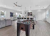 Thumbnail 19 of 38 - A foosball table is in the middle of a room with a couch and a fan.