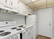 Thumbnail 19 of 31 - A white kitchen with a stove top oven and a refrigerator.