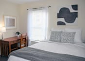 Thumbnail 36 of 38 - A bedroom with a bed, desk, chair, and a painting on the wall.
