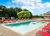 Thumbnail 20 of 22 - Community pool with red sun loungers and yellow umbrella at Southwind Apartments in Richland, MS.