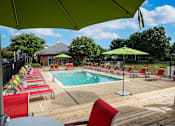 Thumbnail 18 of 22 - Community pool area with red chairs and green umbrellas at Southwind Apartments in Richland, MS.