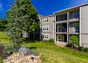Thumbnail 17 of 39 - A large grey rock sits in a bed of small rocks in front of a grey apartment building.