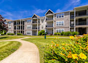 Thumbnail 35 of 39 - A sunny day at a residential apartment complex with a walkway and greenery.