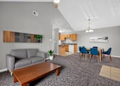 Thumbnail 7 of 18 - A living room with a grey couch, a wooden coffee table, and a dining table with chairs.