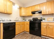 Thumbnail 4 of 21 - A kitchen with wooden cabinets and black appliances.