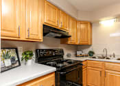 Thumbnail 2 of 21 - A kitchen with wooden cabinets and black appliances.