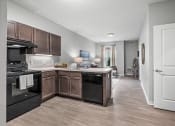 Thumbnail 5 of 19 - a kitchen with wooden cabinets and black appliances and a hallway to a living room
