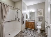 Thumbnail 14 of 35 - A bathroom with a white toilet, a white bathtub, a wooden cabinet, and a rug on the floor.