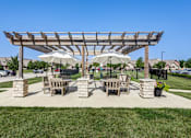 Thumbnail 34 of 35 - A wooden pergola with two umbrellas provides shade for a picnic table and chairs.