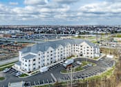 Thumbnail 16 of 20 - A large white building with a grey roof is surrounded by a parking lot.