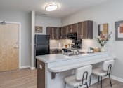 Thumbnail 7 of 20 - A kitchen with a black fridge, white countertop, and brown cabinets.