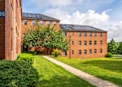 Thumbnail 12 of 14 - A red brick building with a black roof and solar panels on the roof.