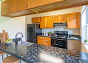 Thumbnail 5 of 14 - A kitchen with a black granite countertop and wooden cabinets.